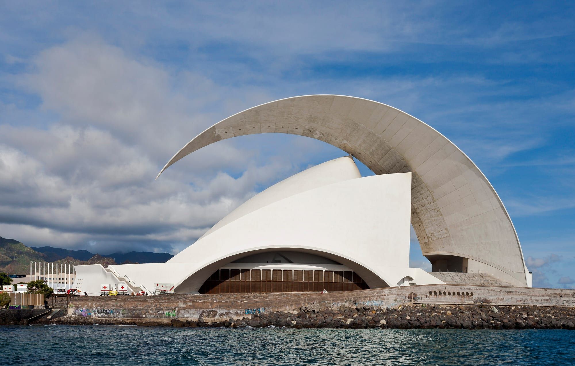 The white Auditorio de Tenerife concert hall with its curved wing-shaped roof on the seafront of Santa Cruz de Tenerife, mountains in the background
